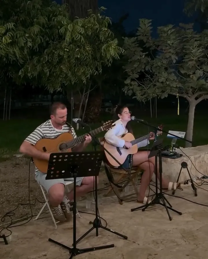 צמד אקוסטי מנגן בחצר מתחת לעצים בלילה